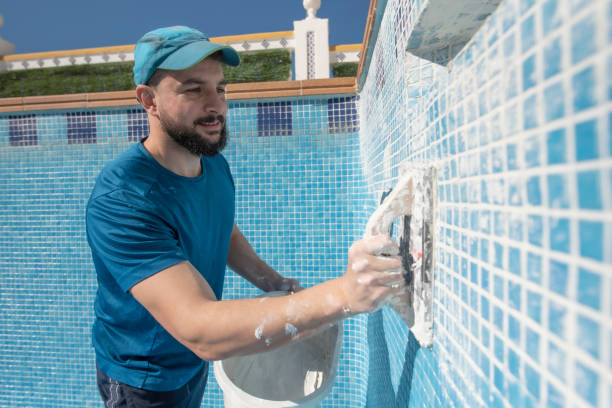 Bearded man spreads the cement grout on the pool tile to waterproof it, preparing pool for summer Man spreads the cement grout on the pool tile to waterproof it pool stock pictures, royalty-free photos & images