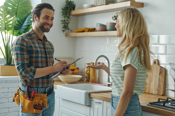 Beautiful young woman talking to male plumber Beautiful young woman talking to male plumber while standing at the kitchen plumbing stock pictures, royalty-free photos & images