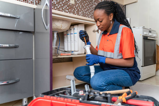 Black female plumber at work Black plumber in uniform fixing kitchen sink she is sitting on the floor in kitchen and fixing pipe plumbing stock pictures, royalty-free photos & images