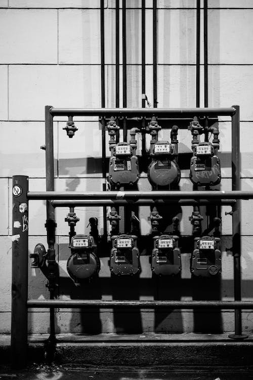 Free Black and white of aged gas meters attached to thin iron pipes near wall Stock Photo