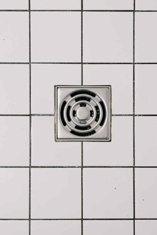 Free Top view of white ceramic tile floor with stainless steel square shaped cover of drain in contemporary shower Stock Photo