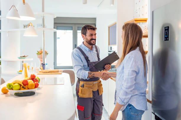 It's a pleasure doing business with you Young Woman Shaking Hands To Male Plumber With Clipboard In Kitchen Room plumbing services stock pictures, royalty-free photos & images