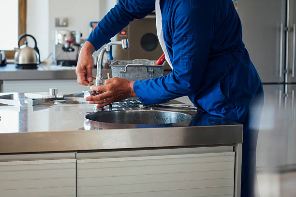 Repairman at Work A shot of a man's hands working on a kitchen sink. He is wearing blue overalls with his tool kit in the background. plumbing services stock pictures, royalty-free photos & images