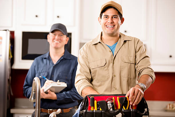 Service Industry: Two multi-ethnic repairmen work at customer's home. Caucasian and Hispanic repairmen or blue collar/service industry workers make service/house call at customer's home kitchen. One holds his tool box filled with work tools. Other worker holds a clipboard in background. Inspector, exterminator, electrician, plumber, repairmen. plumbing team stock pictures, royalty-free photos & images