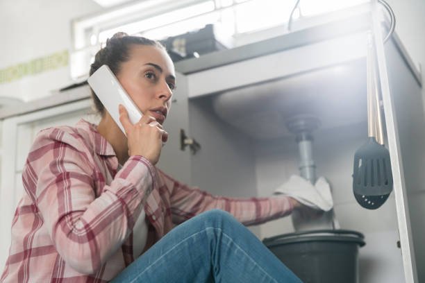 Woman at home calling a plumber about a leaking pipe in her sink Latin American woman at home calling a plumber about a leaking pipe in her sink and looking very worried plumbing stock pictures, royalty-free photos & images