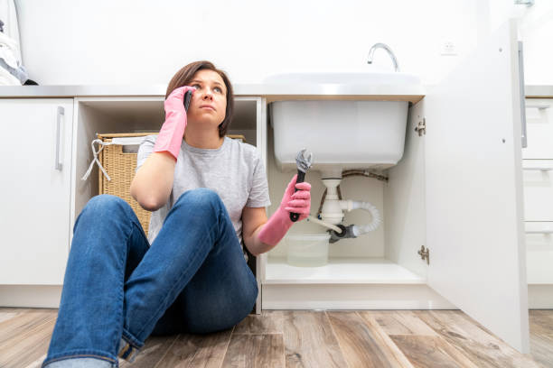 Woman sitting near leaking sink in laundry room calling for help Woman sitting near leaking sink calling for help plumbing stock pictures, royalty-free photos & images
